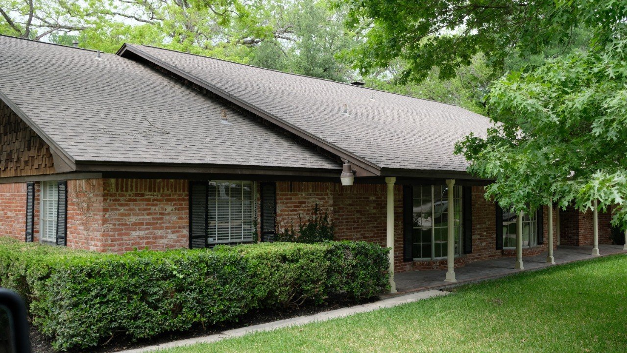 Brick residential exterior with greenery and trees.